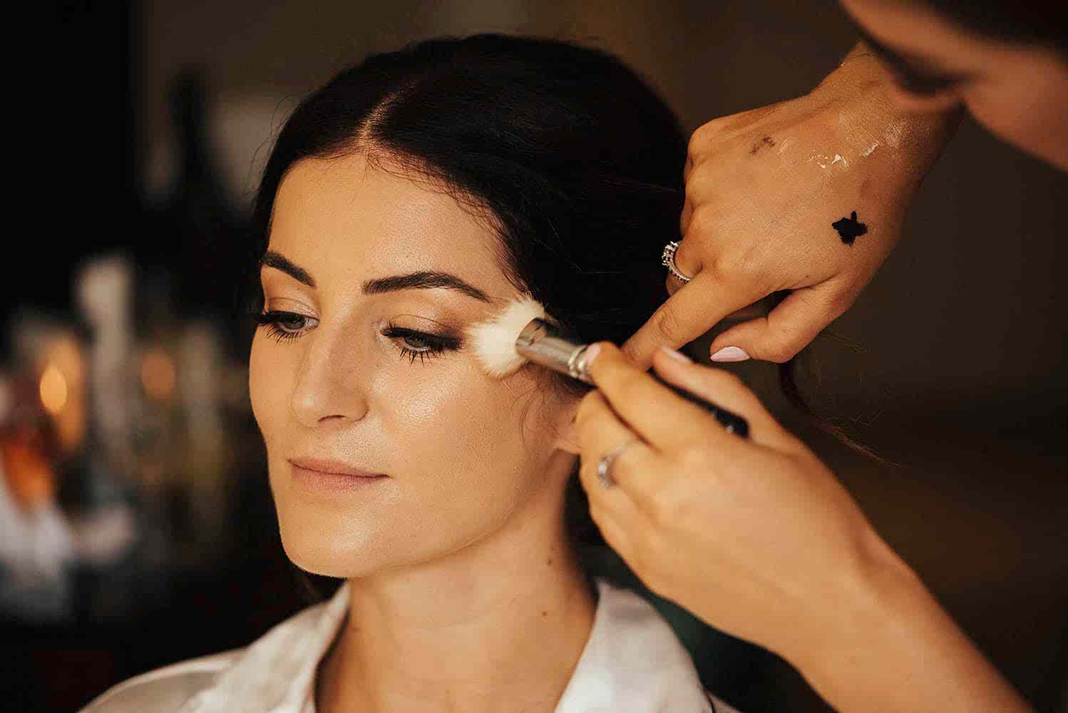 makeup artist applying highlighter to bride